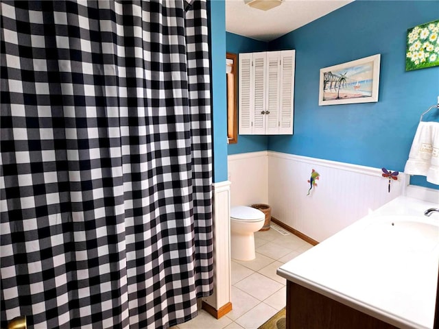 bathroom featuring a sink, toilet, wainscoting, and tile patterned flooring