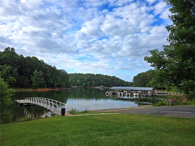 view of dock featuring a forest view, a water view, and a lawn