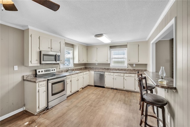 kitchen with a wealth of natural light, appliances with stainless steel finishes, ornamental molding, and light wood finished floors