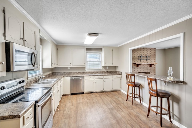 kitchen featuring crown molding, a breakfast bar area, light wood-style floors, stainless steel appliances, and a sink