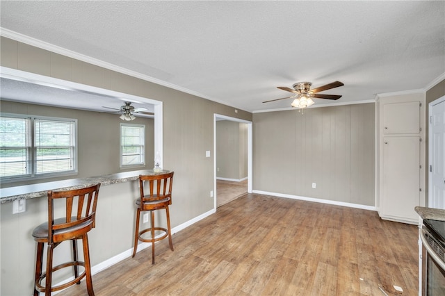 interior space featuring crown molding, ceiling fan, a breakfast bar, light wood-type flooring, and a textured ceiling