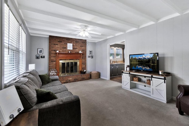 living area featuring beamed ceiling, plenty of natural light, a fireplace, and ceiling fan