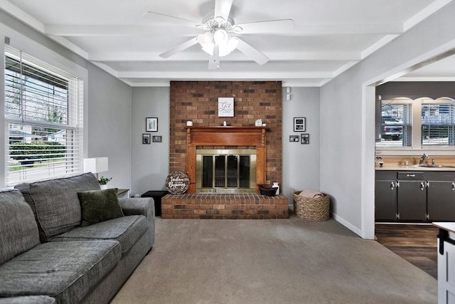 living area with a brick fireplace, beamed ceiling, baseboards, and ceiling fan