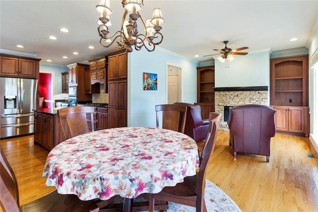 dining space featuring ornamental molding, ceiling fan with notable chandelier, recessed lighting, a fireplace, and light wood finished floors