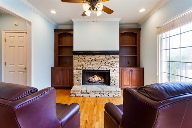 living area featuring wood finished floors, recessed lighting, a fireplace, crown molding, and ceiling fan