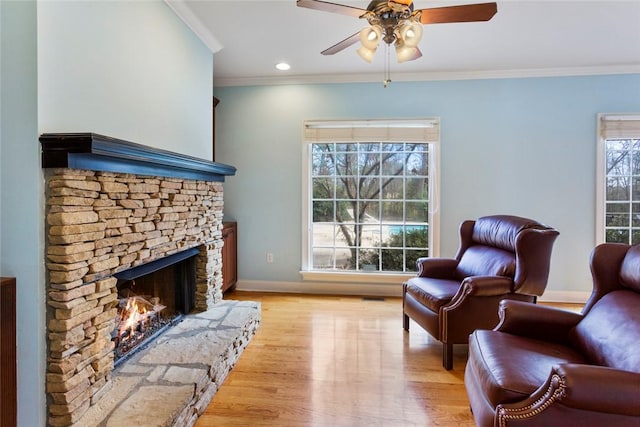 living room featuring baseboards, light wood-style flooring, a fireplace, ceiling fan, and crown molding