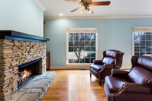 living area with crown molding, baseboards, a fireplace, light wood-style floors, and a ceiling fan