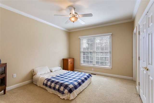 carpeted bedroom with a closet, baseboards, ornamental molding, and a ceiling fan