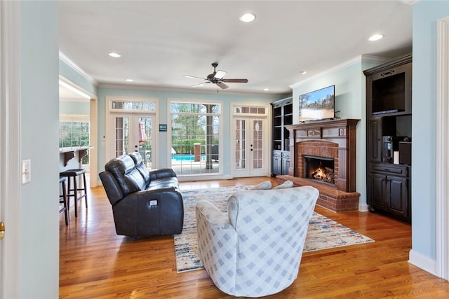 living room featuring a ceiling fan, french doors, light wood-type flooring, and a fireplace