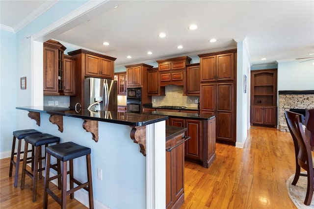 kitchen featuring a breakfast bar, a peninsula, black appliances, light wood-style floors, and crown molding