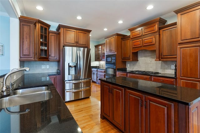 kitchen featuring black appliances, light wood-style flooring, a sink, crown molding, and glass insert cabinets