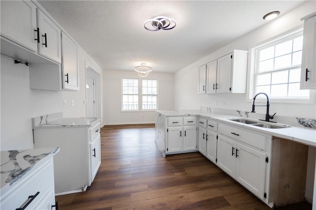 kitchen with dark wood-type flooring, light stone counters, a peninsula, white cabinetry, and a sink