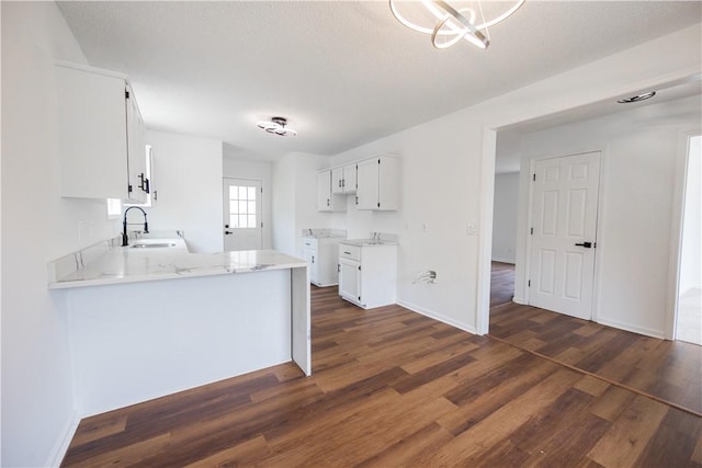 kitchen with dark wood finished floors, white cabinets, light stone counters, and a sink