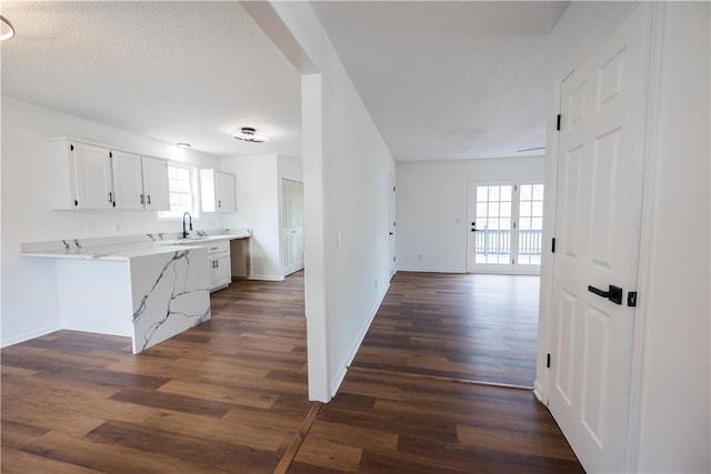 kitchen with a sink, light stone countertops, white cabinetry, and dark wood-style flooring