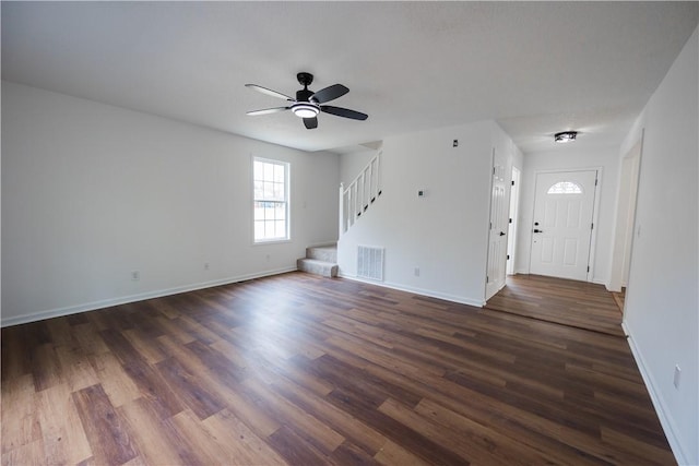 unfurnished living room with stairway, dark wood-style floors, a ceiling fan, visible vents, and baseboards