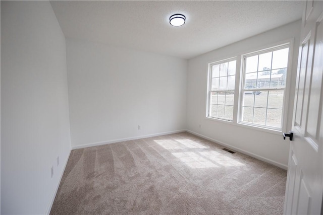 spare room featuring visible vents, light carpet, a textured ceiling, and baseboards