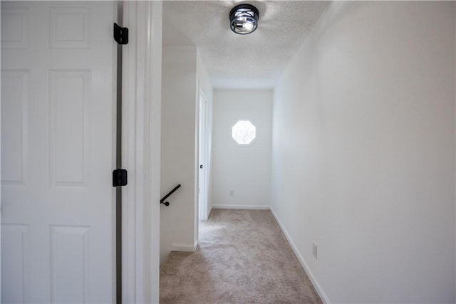 corridor featuring light colored carpet, baseboards, and a textured ceiling