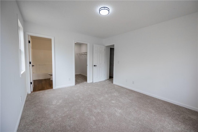 unfurnished bedroom with a spacious closet, carpet, baseboards, and a closet