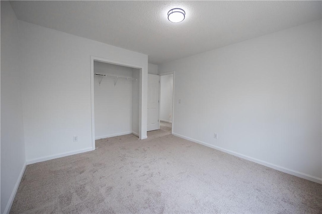 unfurnished bedroom featuring a textured ceiling, baseboards, a closet, and light carpet