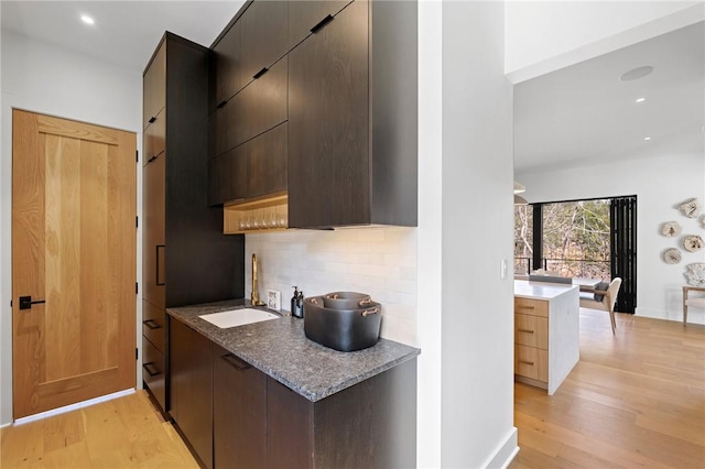 kitchen with light wood-type flooring, modern cabinets, a sink, backsplash, and dark brown cabinets