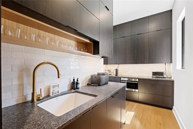 kitchen with a sink, backsplash, oven, and open shelves