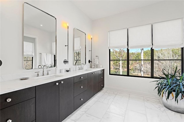 full bath with double vanity, marble finish floor, baseboards, and a sink