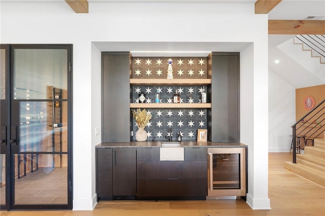 bar featuring beverage cooler, a dry bar, stairs, and wood finished floors