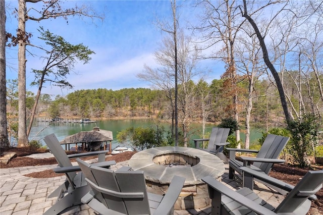 view of patio with a view of trees, a water view, and an outdoor fire pit