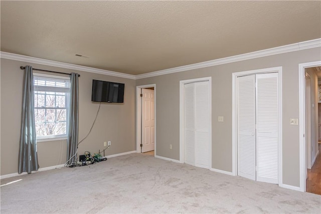 unfurnished bedroom featuring carpet, multiple closets, and ornamental molding