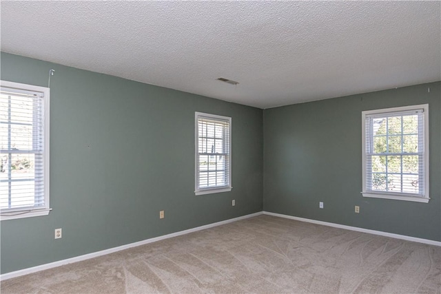 unfurnished room with visible vents, baseboards, light colored carpet, and a textured ceiling