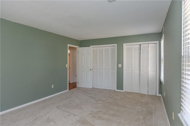 unfurnished bedroom with a textured ceiling, baseboards, carpet, and multiple closets