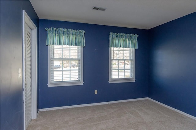 empty room featuring baseboards, visible vents, and light carpet