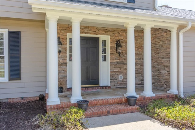 doorway to property with a porch, stone siding, and a shingled roof