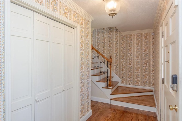 stairway featuring wallpapered walls, wood finished floors, baseboards, and a textured ceiling