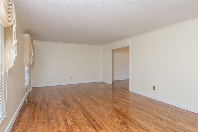 spare room featuring crown molding, baseboards, light wood-type flooring, and a textured ceiling