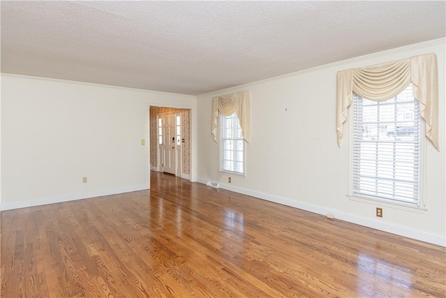 empty room with a textured ceiling, wood finished floors, and crown molding