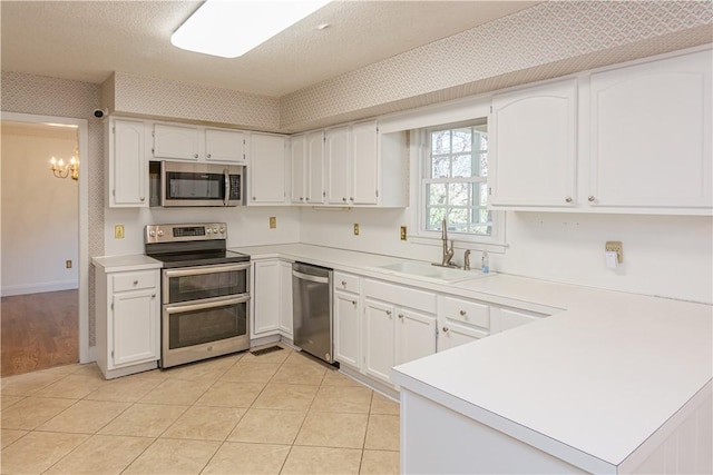 kitchen with a sink, an inviting chandelier, appliances with stainless steel finishes, a peninsula, and wallpapered walls