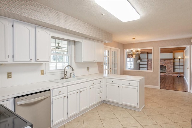 kitchen with wallpapered walls, a chandelier, stainless steel dishwasher, white cabinetry, and a sink