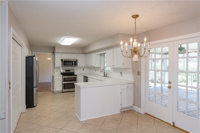 kitchen featuring wallpapered walls, a peninsula, an inviting chandelier, stainless steel appliances, and white cabinetry