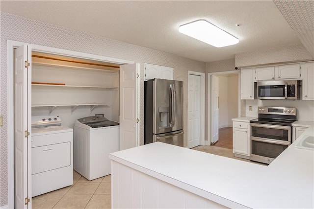 kitchen featuring wallpapered walls, a peninsula, appliances with stainless steel finishes, independent washer and dryer, and white cabinetry