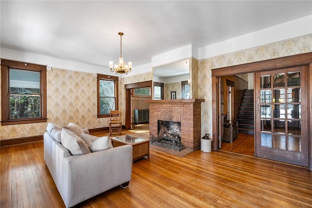 living area featuring wallpapered walls, baseboards, hardwood / wood-style floors, a fireplace, and an inviting chandelier