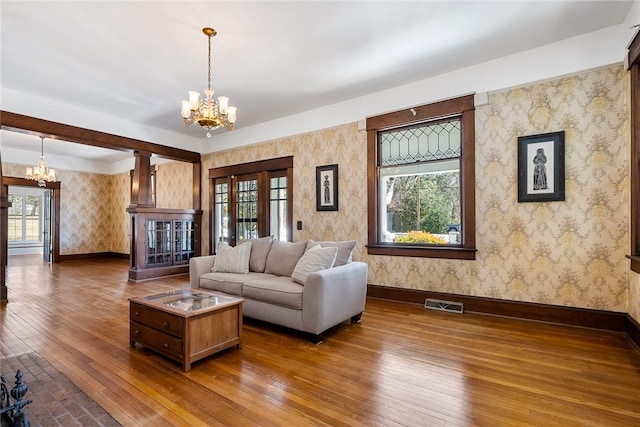 living area with visible vents, wallpapered walls, baseboards, hardwood / wood-style flooring, and a notable chandelier