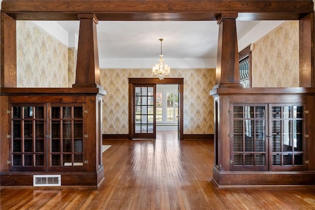 interior space with visible vents, wallpapered walls, a chandelier, decorative columns, and hardwood / wood-style flooring