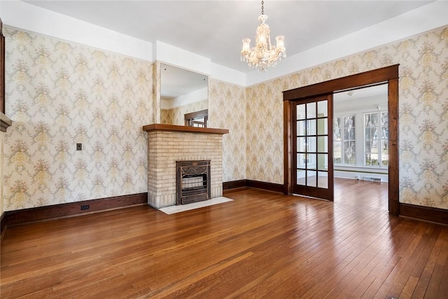 unfurnished living room featuring hardwood / wood-style flooring, a fireplace, wallpapered walls, baseboards, and a chandelier