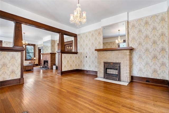 living area featuring wallpapered walls, an inviting chandelier, a fireplace, and hardwood / wood-style floors