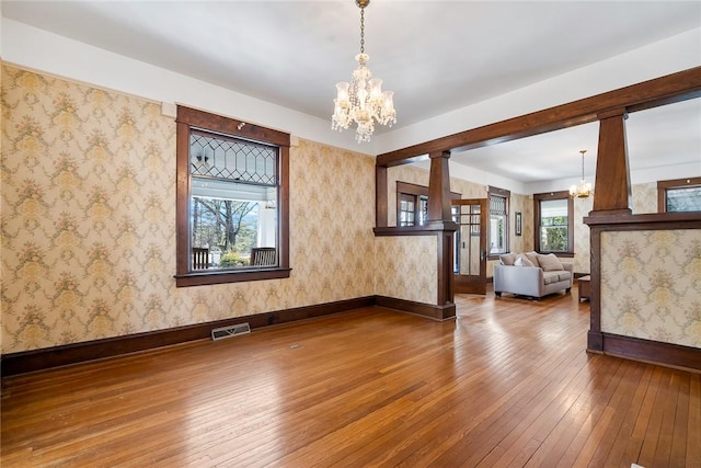 unfurnished room featuring a wealth of natural light, visible vents, hardwood / wood-style flooring, an inviting chandelier, and wallpapered walls