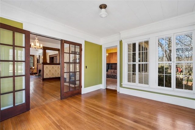 empty room with hardwood / wood-style floors, baseboards, french doors, crown molding, and a chandelier