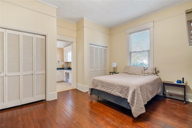 bedroom featuring two closets, hardwood / wood-style flooring, baseboards, and ornamental molding