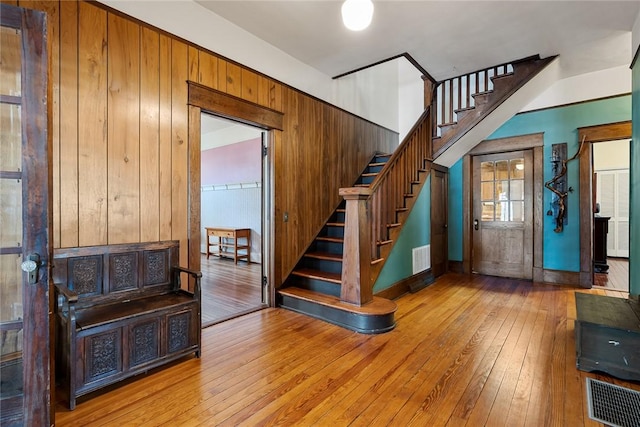 foyer with visible vents, hardwood / wood-style floors, stairs, and wood walls