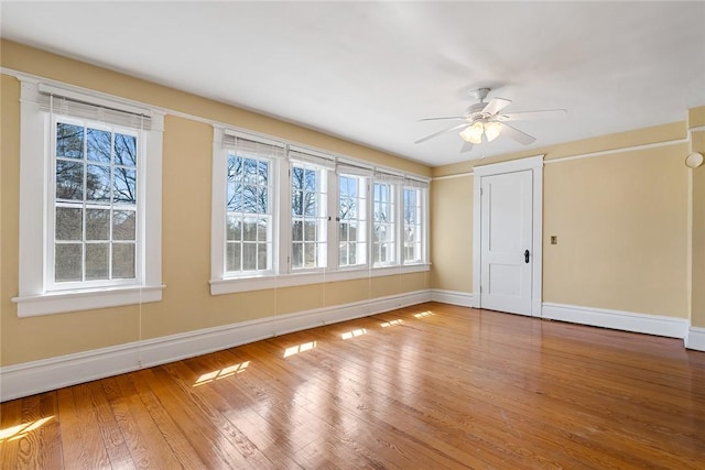 spare room featuring a ceiling fan, plenty of natural light, wood finished floors, and baseboards